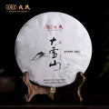 Chinese pu-erh tea cake wrapped in white paper with mountain artwork, displayed on a wooden stand