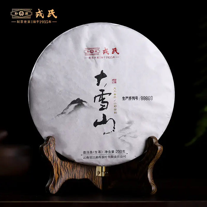Chinese pu-erh tea cake wrapped in white paper with mountain artwork, displayed on a wooden stand