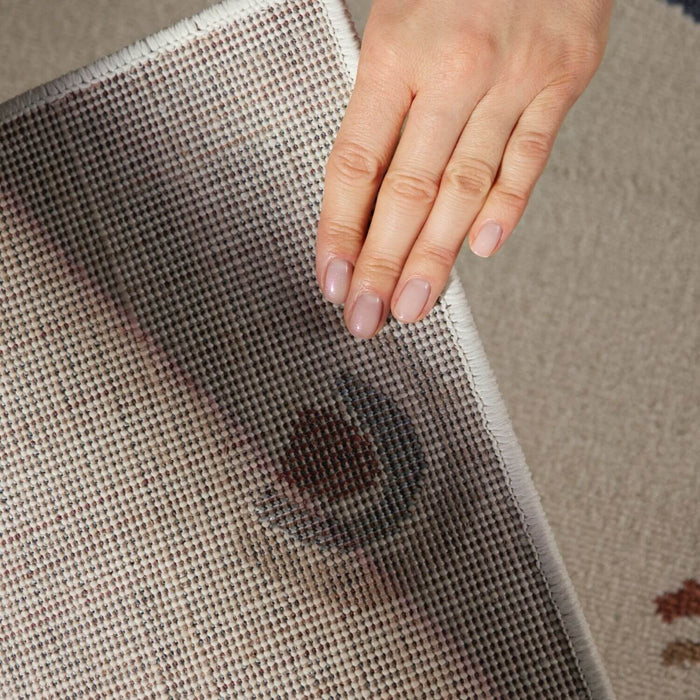 Hand holding a piece of fabric with a dark stain on a neutral background