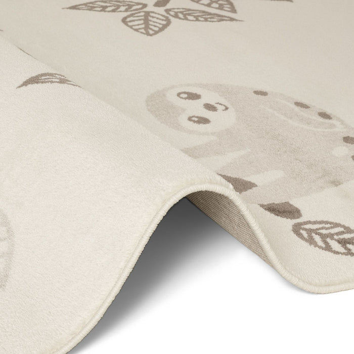 Close-up of a beige play mat with sloth and leaf designs on a white background
