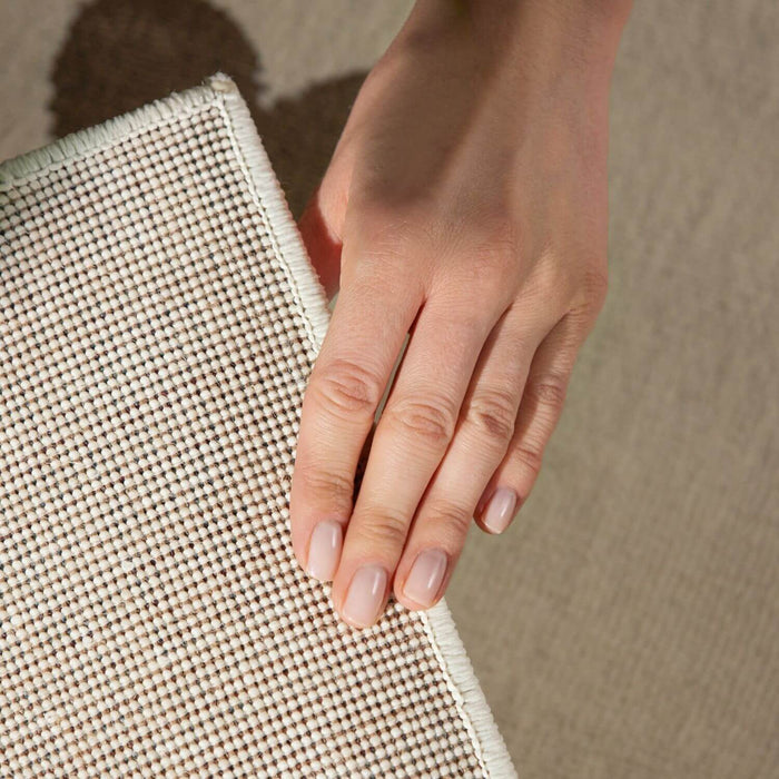 Hand holding a textured beige mat on a neutral background