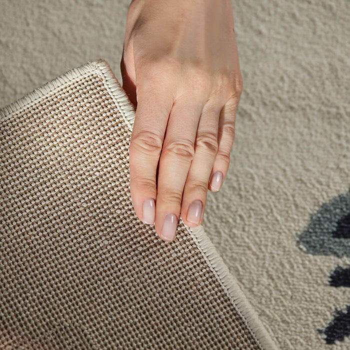 Hand holding a textured beige rug corner on a neutral background