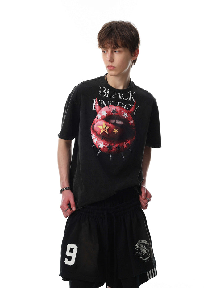 Black graphic tee with red devil lips, stars, and distressed punk text on a model against a white background