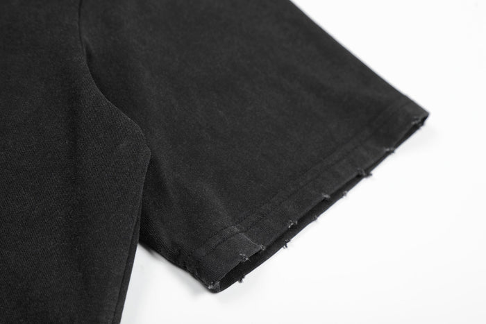 Black distressed graphic tee sleeve detail with raw-cut hem, showcasing punk streetwear style and textured cotton fabric