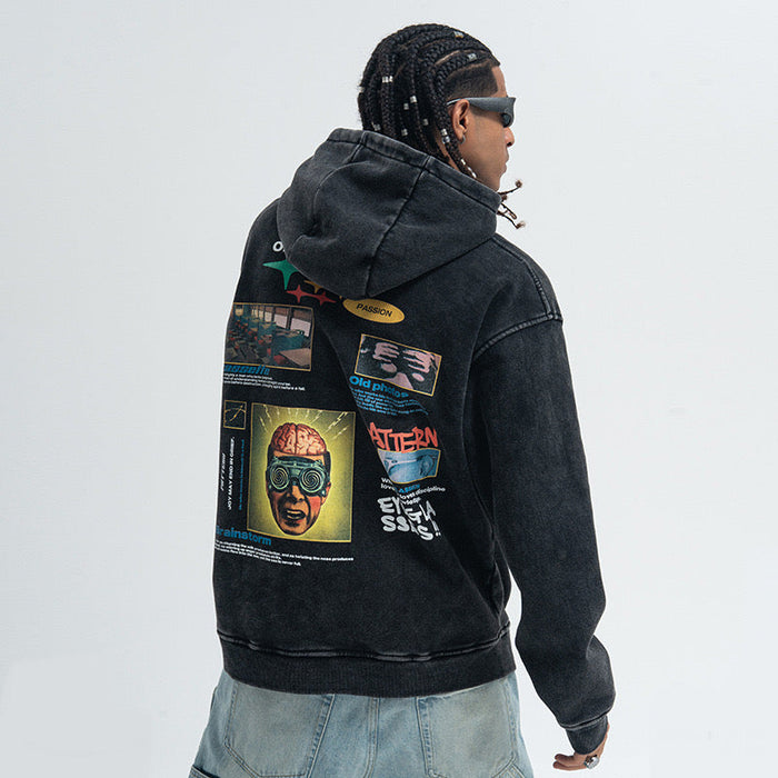 Man wearing an oversized black washed pullover hoodie with a bold graphic collage print on the back, paired with light blue j