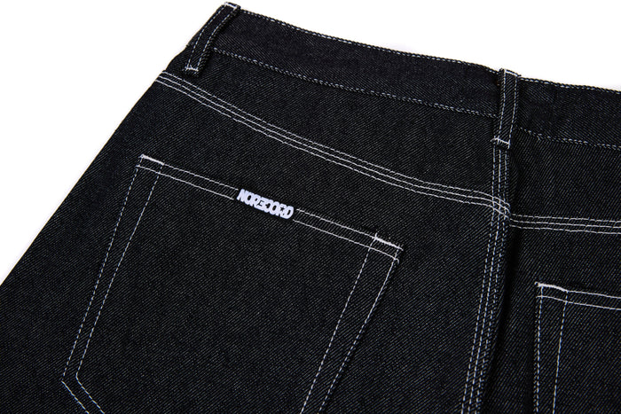 Back pocket of black denim jeans with white stitched logo detail