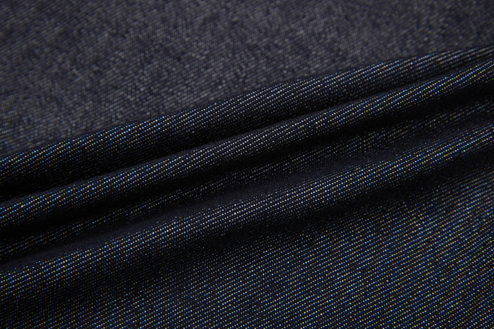 Close-up of dark denim fabric with visible twill weave and folds