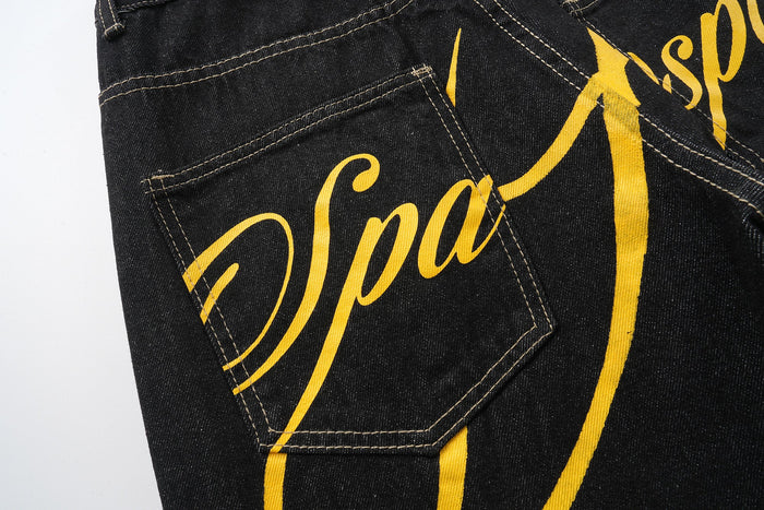 Back pocket close-up of black jeans showing yellow script print and stitching