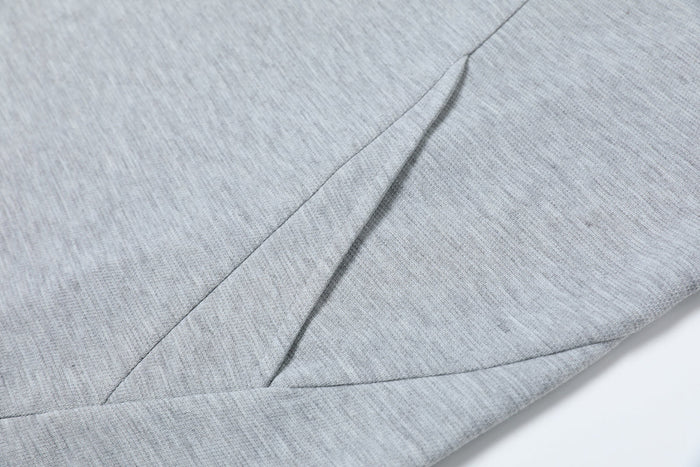 Close-up of light gray oversized tee fabric with sharp geometric seam detailing and a structured minimalist cut