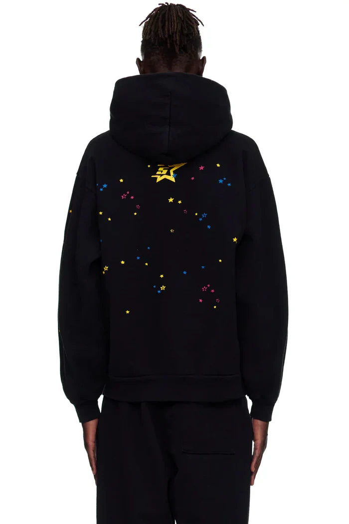 Person wearing a black Sp5der “Hares the Slime” Hoodie, a 440GSM heavyweight pullover with a spider-web streetwear design, hood up, and colorful star details including a large yellow star on the back.