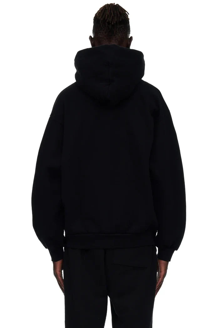A person with short, twisted hair is shown from behind wearing the Sp5der “I Love Sp5der” Hoodie – Black Web 440GSM Heavyweight Streetwear Pullover and black pants against a white background.
