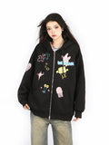 A person wears Seakoff's Kawaii Pastel Cartoon Hoodie, a cute black zip-up with playful embroidered stars and jellyfish. Their long dark hair complements loose-fitting blue jeans against a plain white background.