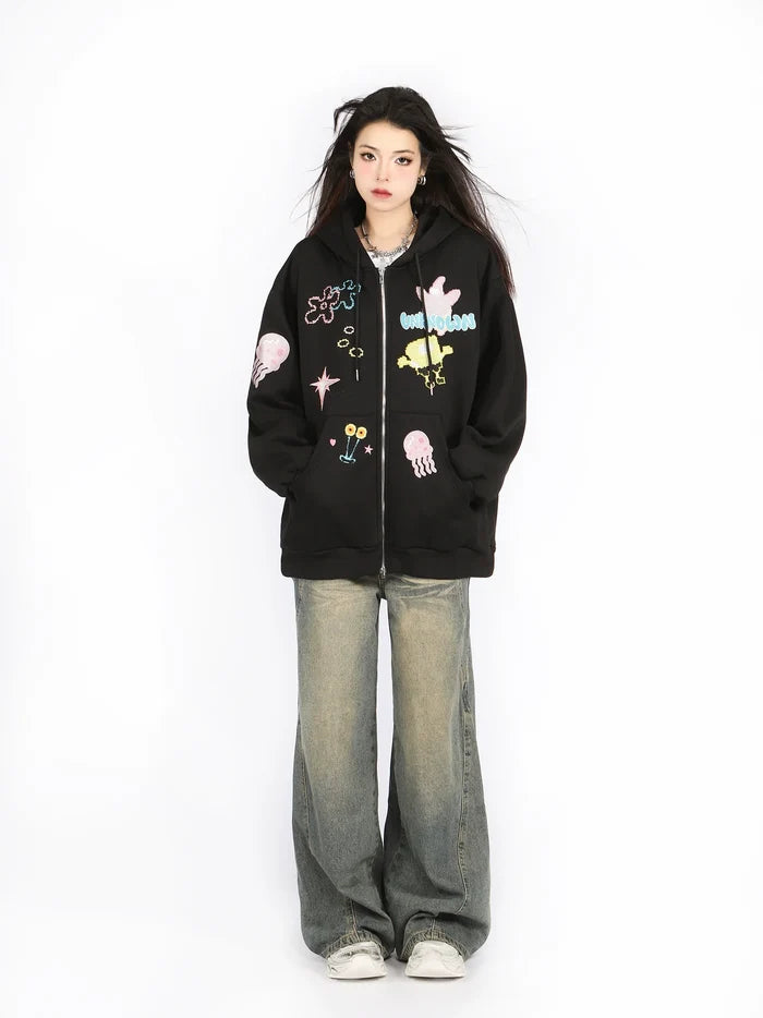 Against a plain white background, a person showcases their anime-inspired fashion with long dark hair, white sneakers, and baggy jeans while wearing Seakoff's Kawaii Pastel Cartoon Hoodie—a cute full-zip hoodie featuring various abstract shapes and playful embroidered designs.