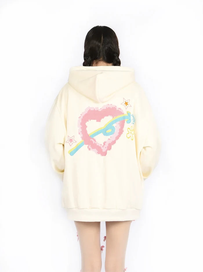 A person with braided hair is wearing Seakoff's Kawaii Pastel Cartoon Hoodie, a cream-colored full-zip hoodie showcasing playful embroidered designs on the back, including a pink pixelated heart, colorful arrow, and small stars. Embracing kawaii fashion, the person faces away from the camera.