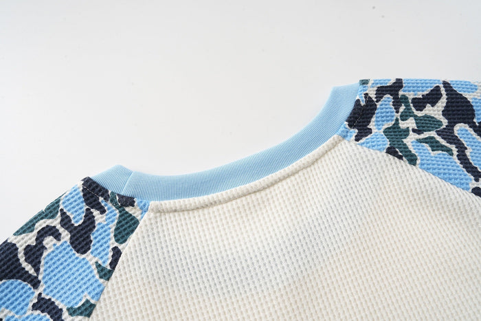 Close-up of a camo raglan graphic T-shirt with light blue ribbed collar and textured waffle knit fabric
