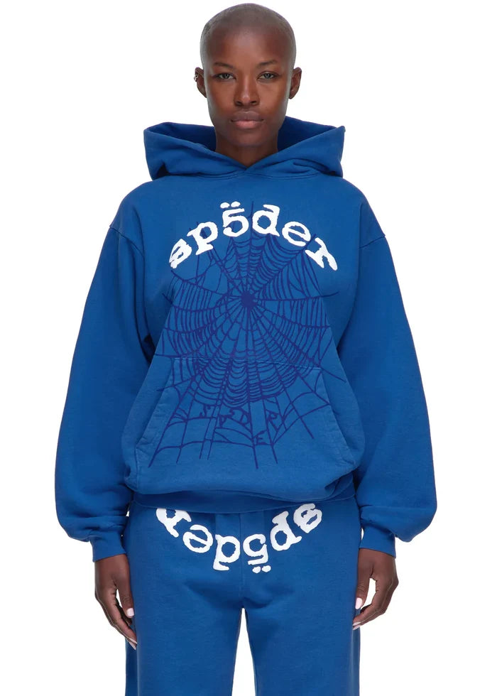 A person wears the Sp5der OG Web Hoodie 440GSM in royal blue—a heavyweight streetwear sweatshirt with a large white spiderweb and "sp5der" print—paired with matching sweatpants featuring the same graphic.