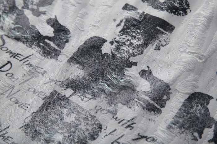 Close-up of white distressed graphic mesh tee with black abstract print and textured patchwork detailing