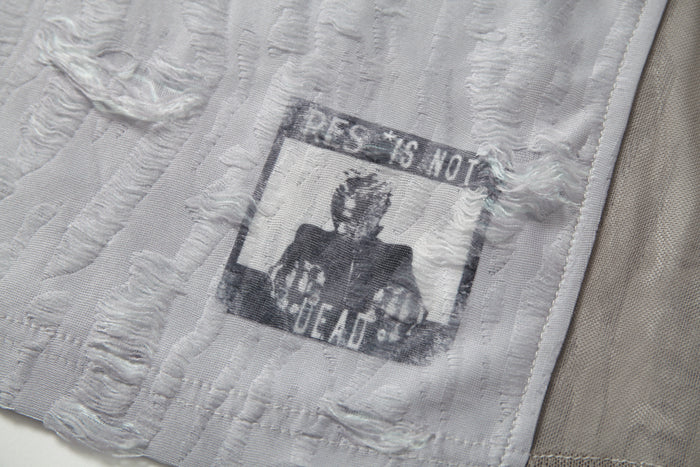 Close-up of a textured white mesh tee with distressed patchwork and faded graphic print detail
