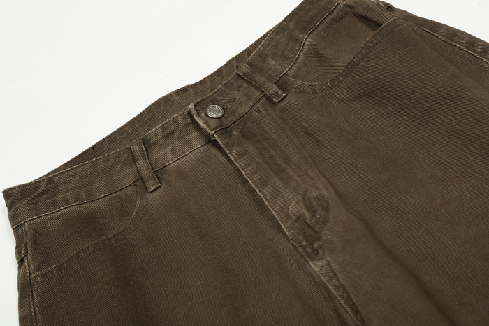 Close-up of brown pants waistband with snap button, belt loops, and worn cotton texture