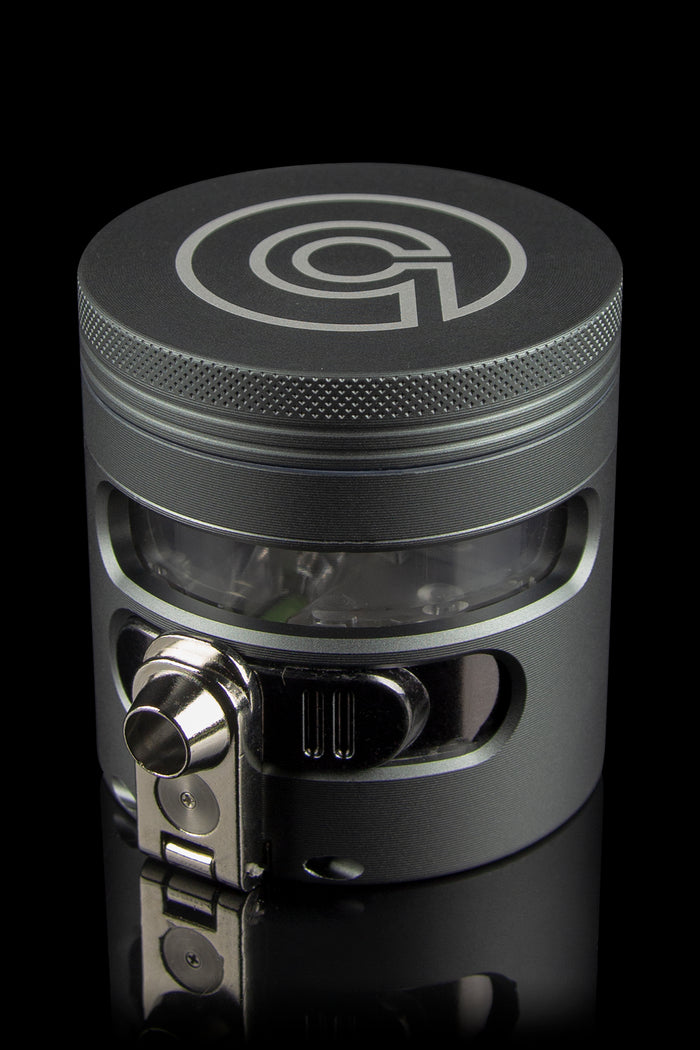 Black metal cannabis grinder with a clear collection chamber visible, displaying green plant material.