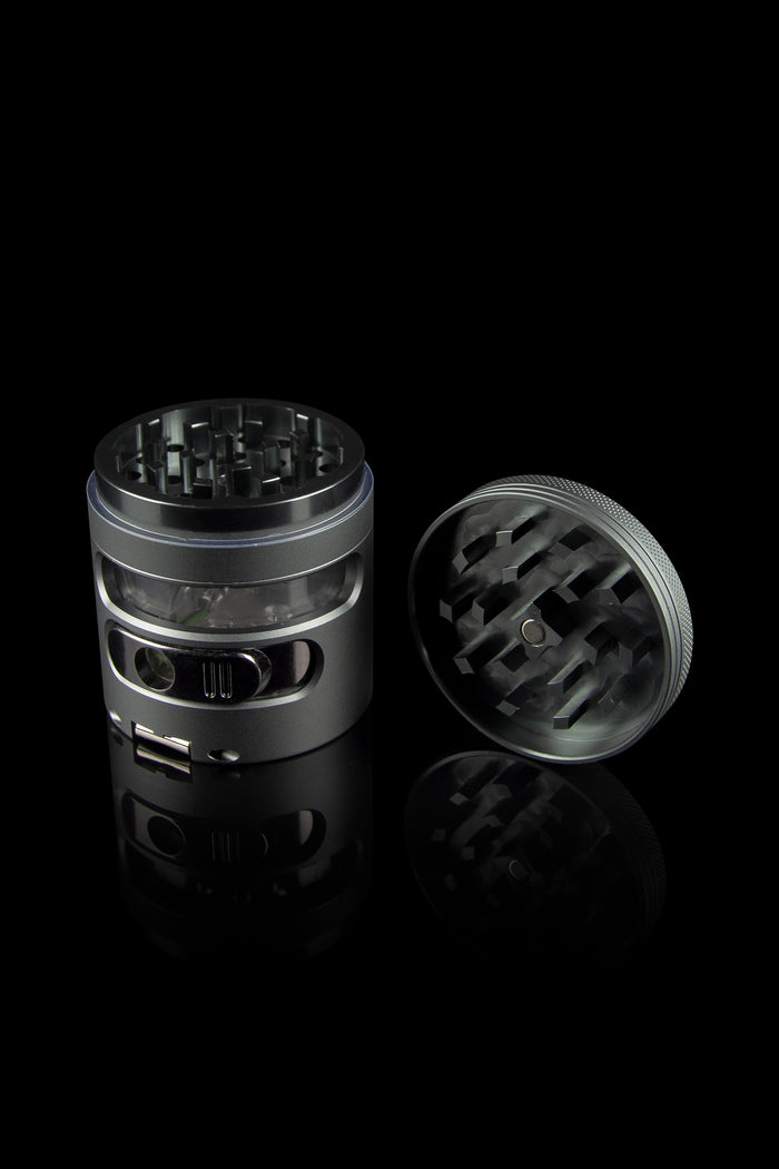 Black cannabis grinder with open lid, reflecting on a dark surface.