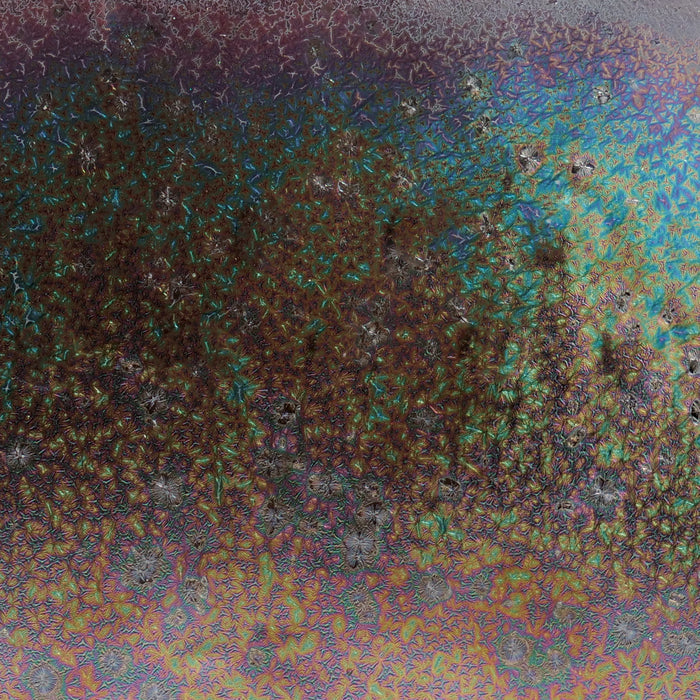 Close-up of Amaco CO-8 Dark Star glaze, dark surface packed with iridescent teal, gold and purple crystals