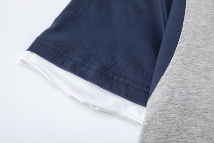 Close-up of a colorblock raglan T-shirt with navy sleeve, white layered hem, and heather gray side panel