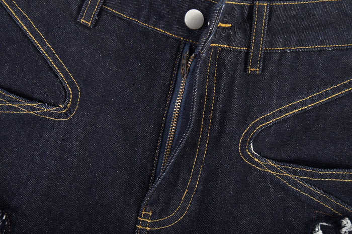 Close-up of the front fly on dark jeans showing zipper, button, and stitched pocket detail