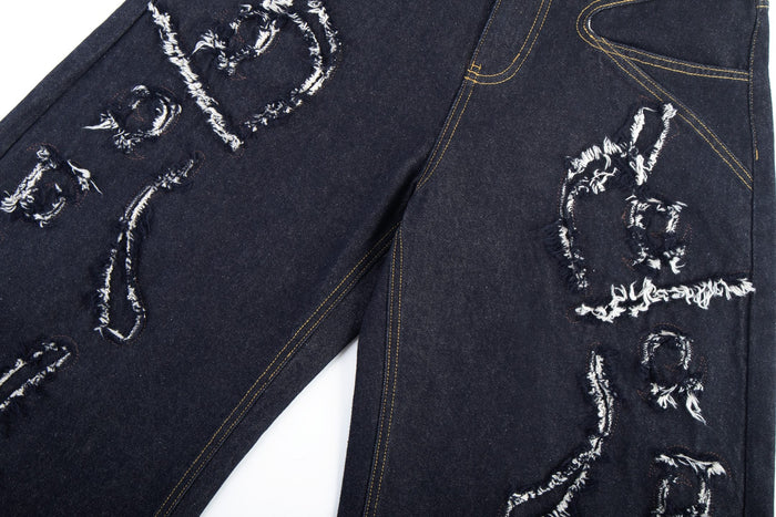 Close-up of distressed flame stitch details across the front legs of dark denim jeans