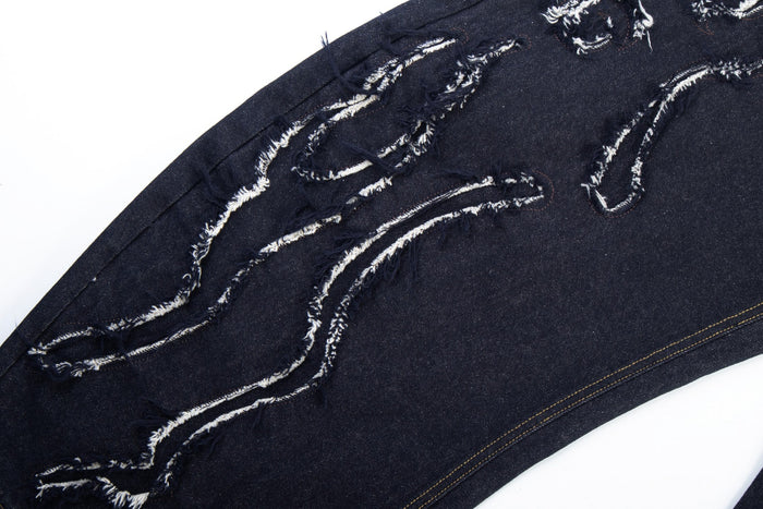 Diagonal close-up of flame-shaped distressing and frayed white stitching on dark jeans leg