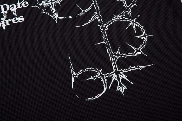 Close-up of black textured polo shirt with white thorny Gothic cross graphic and distressed streetwear lettering