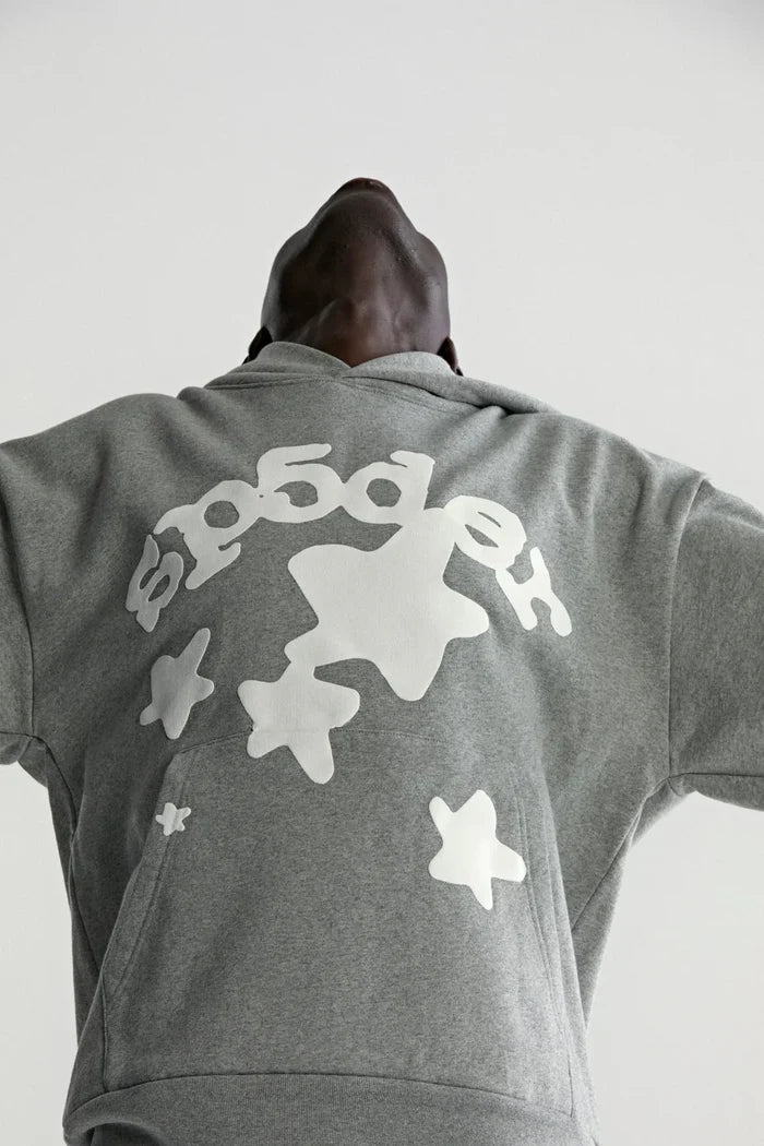 A person wears the Sp5der Stars Hoodie – Grey 440GSM Heavyweight Streetwear Pullover, head tilted back and arms outstretched, viewed from a low angle against a light background.