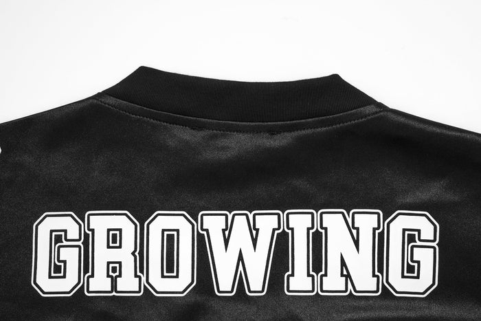 Black metallic varsity mesh jersey tee with ribbed collar and bold white GROWING graphic across the back