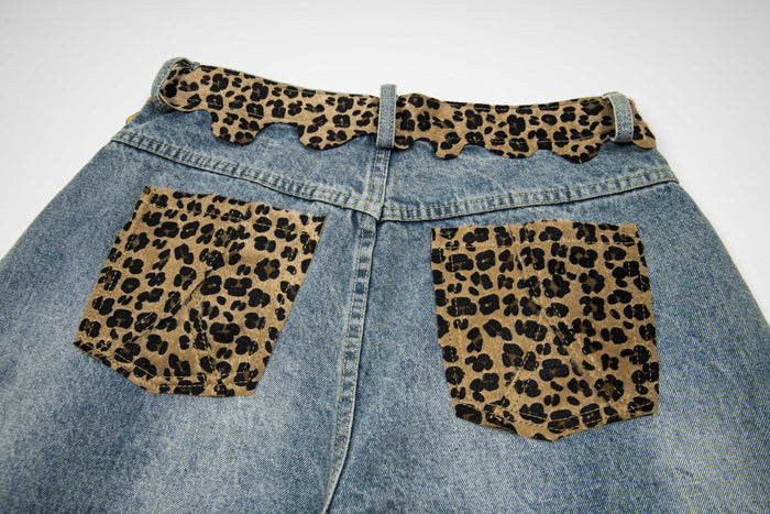 Back upper view of denim shorts with two leopard print patch pockets and scalloped waist trim