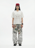Model wearing an oversized white V-neck mesh tee with Los Angeles 24 Respect print, red headwrap, and camo cargo pants