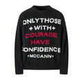 Black fuzzy knit crewneck sweater with bold white and red slogan text reading Only Those With Courage Have Confidence McCann