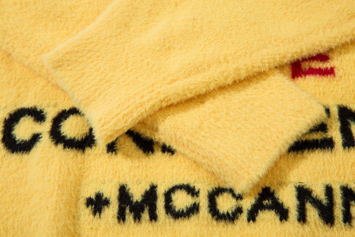 Close-up of yellow fuzzy knit sweater with black and red slogan lettering