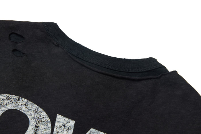 Close-up of a washed black distressed graphic tee with layered neckline and faded white print on soft cotton fabric
