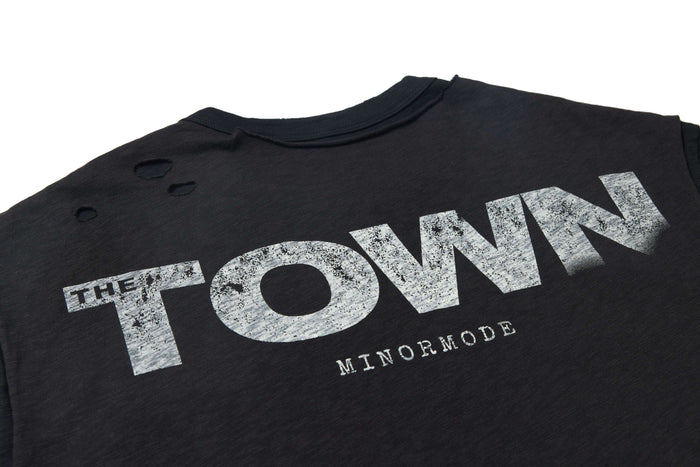 Washed black distressed graphic tee with faded The Town print and torn shoulder details
