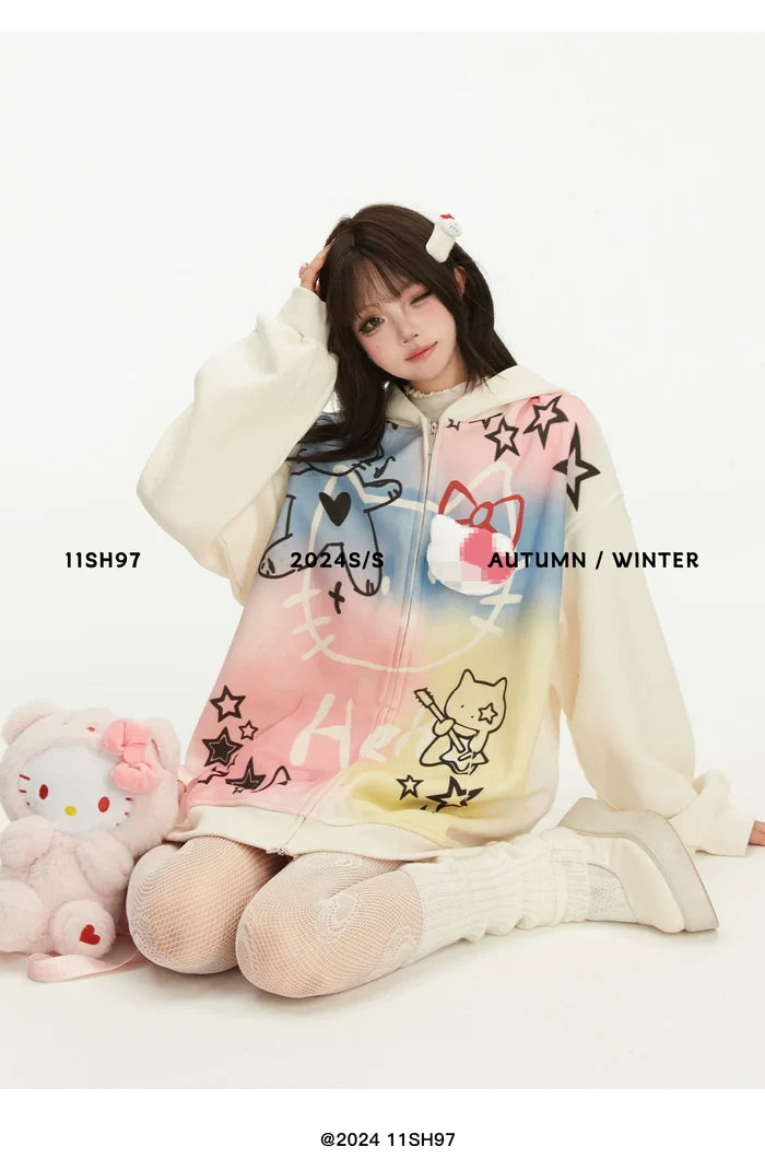 A person sits on the floor in a Seakoff oversized Pastel Cat Graffiti Hoodie, embracing their knees. They're surrounded by a plush toy and have a hair clip in their hair. The plain white background features text overlays promoting Seakoff's kawaii streetwear collection for 2024.
