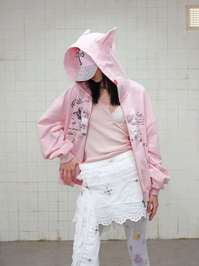Model wearing pink graphic zip hoodie with hood up and matching cap