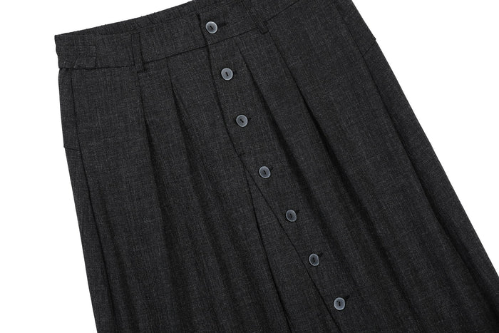 Diagonal close-up of black pants front with pleats and button placket