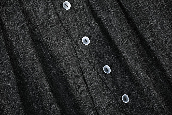 Close-up of black textured fabric with front buttons and pleat seams