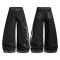 Black wide-leg denim jeans with polka dot waistband and hem cuffs, white script graphic print on right leg, front and back vi