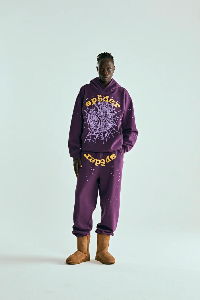 A person stands against a plain background wearing the Sp5der Web Hoodie – Deep Purple & Yellow 440GSM Heavyweight Oversized Streetwear Pullover, sweatpants, and tan boots—ideal for luxury streetwear and Y2K fashion fans.