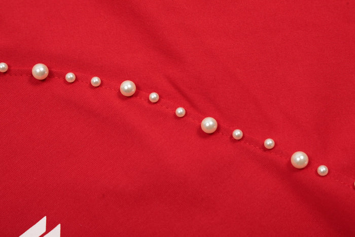 Close-up of a red studded raglan cotton tee with pearl-like accents and visible seam detail