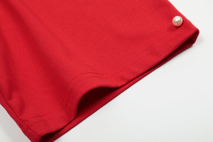 Close-up of a red studded raglan cotton tee sleeve with pearl button detail and visible hem stitching