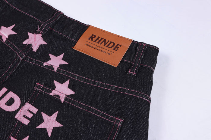 Close-up of the back waist label and pink star embroidery on black denim pants