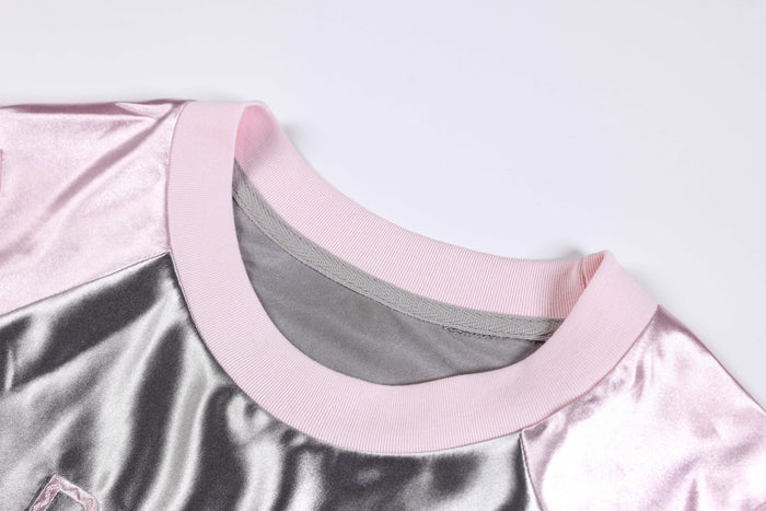 Pink metallic varsity jersey tee with ribbed crew neck and shiny silver satin panels on a white background
