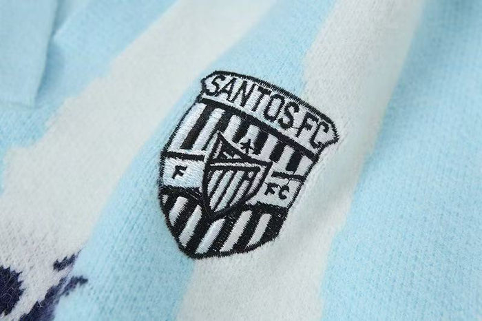 Close-up of Santos FC crest on light blue striped knit polo sweater